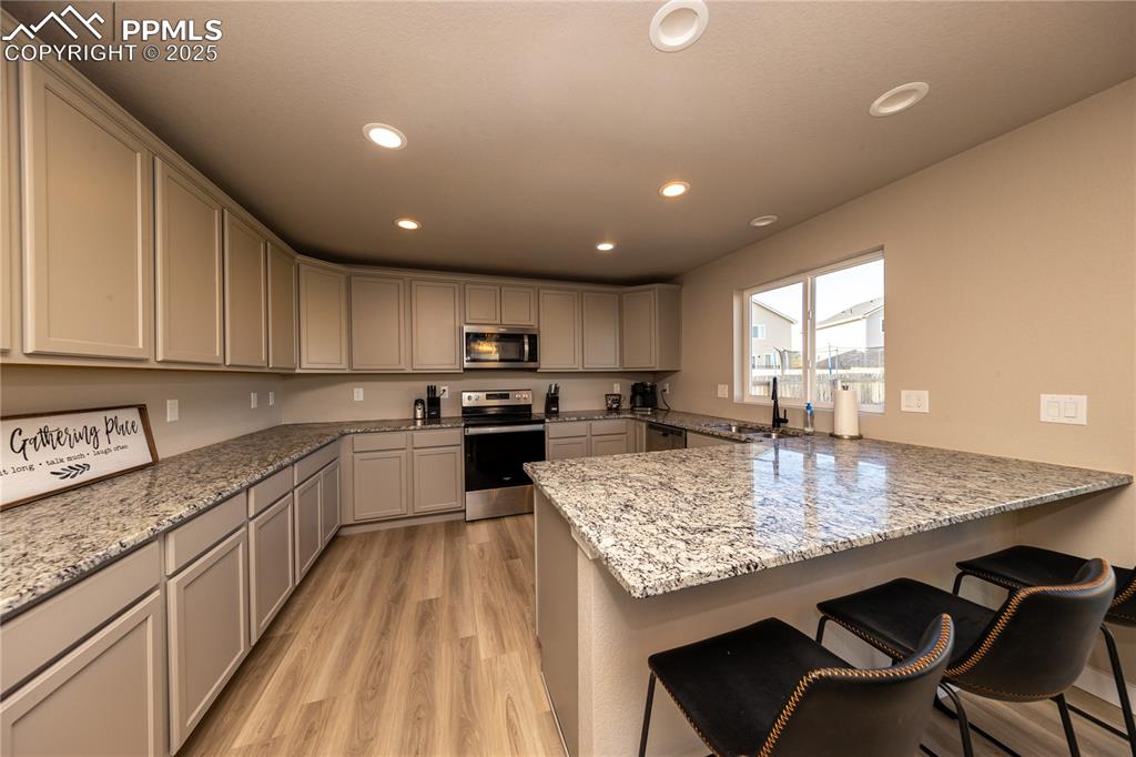 Image 11 of 32: Kitchen with a breakfast bar, light stone countertops, appliances with stai