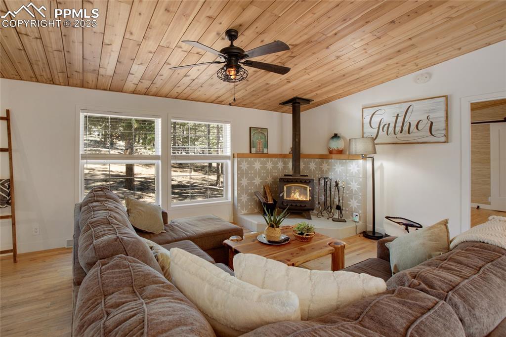 Image 11 of 47: Living area with lofted ceiling, a wood stove, a ceiling fan, wood ceiling,
