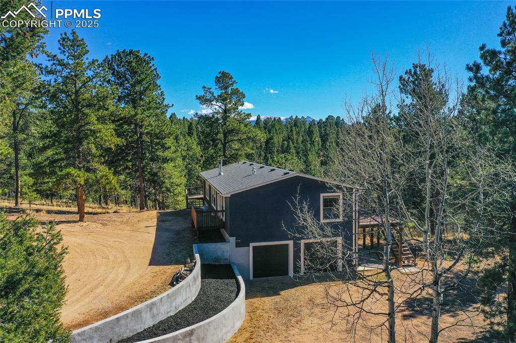 Image 4 of 47: View of side of home featuring a wooded view, dirt driveway, and stucco sid