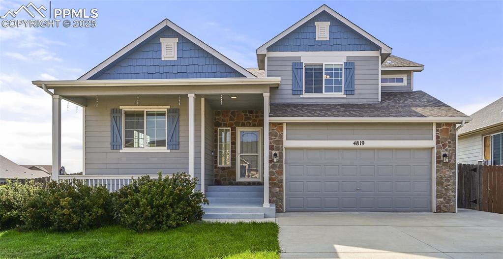 Caption: View of front facade with stone siding, covered porch, an attached garage, and concrete driveway