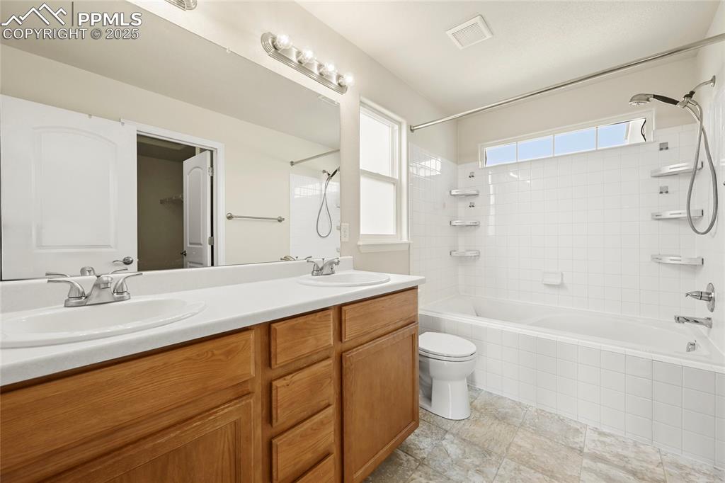 Image 16 of 28: Bathroom with tiled shower / bath combo and double vanity