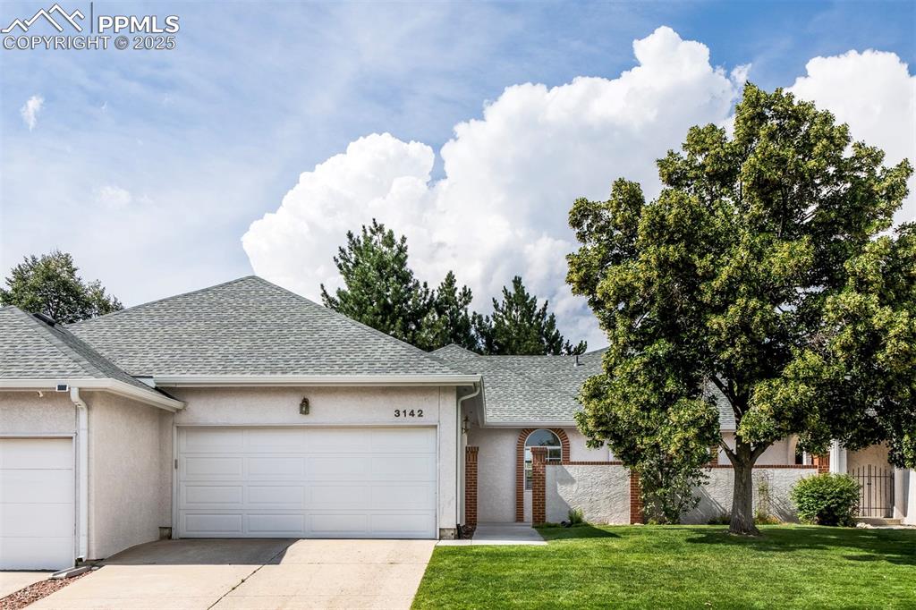 Caption: View of front facade featuring roof with shingles, driveway, a garage, stucco siding, and a front ya