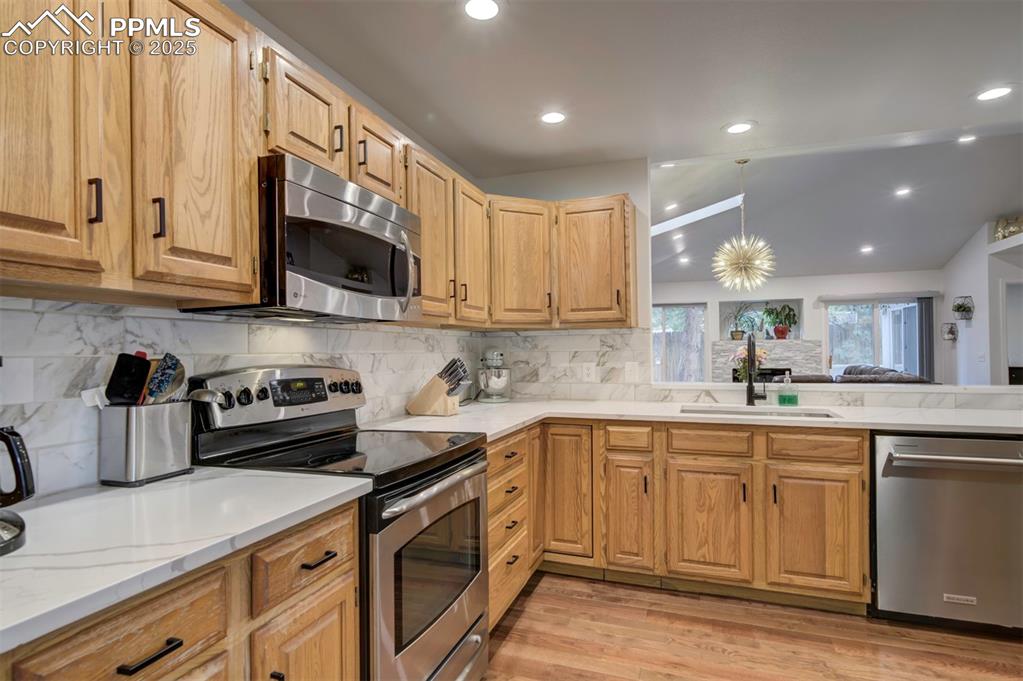 Image 23 of 40: Kitchen with appliances with stainless steel finishes, vaulted ceiling, lig
