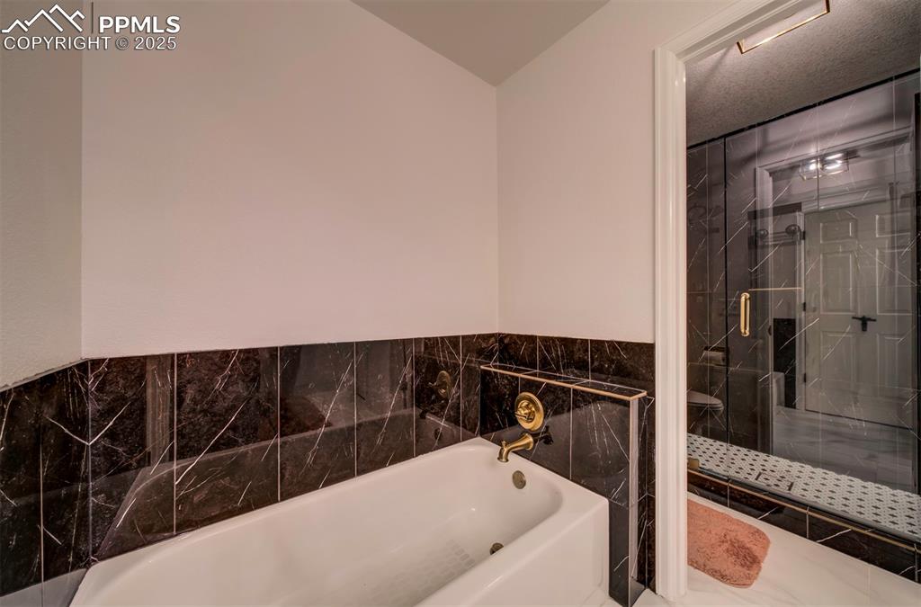 Image 33 of 40: Bathroom with a garden tub, a shower stall, and tile walls