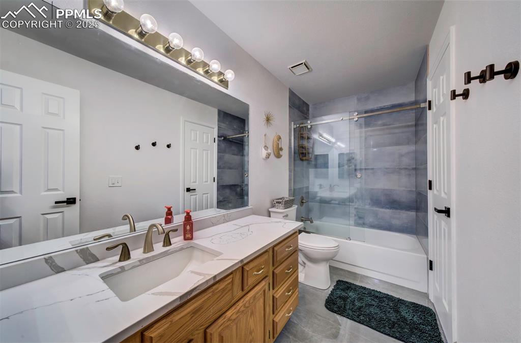 Image 40 of 40: Bathroom with vanity, shower / bath combination with glass door, and tile p
