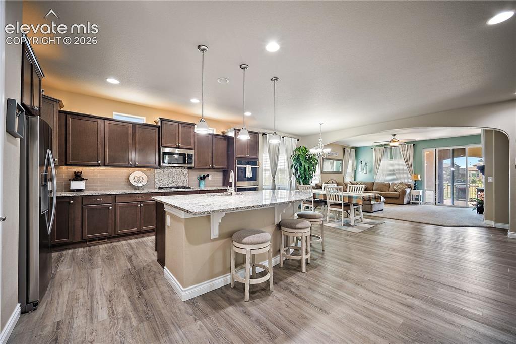 Image 8 of 49: spacious kitchen with large island. Granite, SS and laminate wood flooring.
