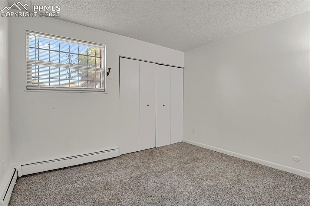Image 13 of 17: Unfurnished bedroom with a textured ceiling, a baseboard radiator, carpet f