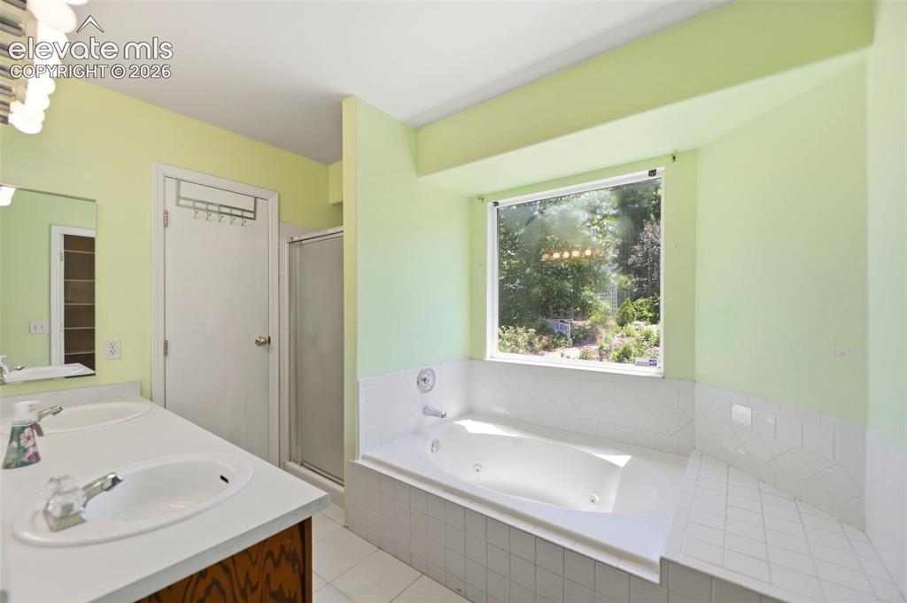 Image 18 of 50: Bathroom featuring a large soaking tub with a tiled surround, a separate sh
