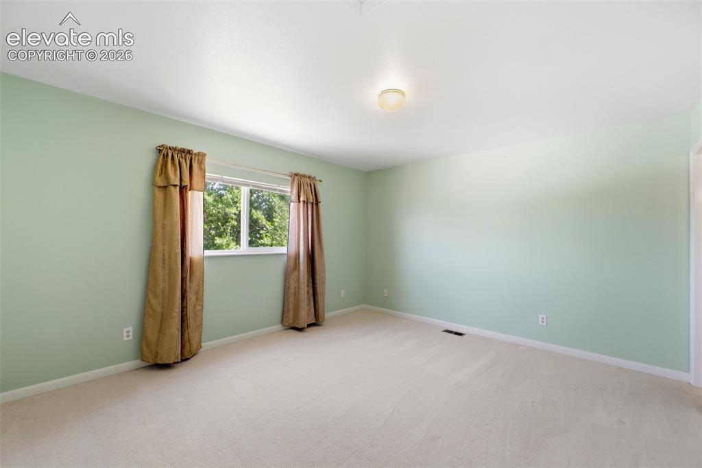 Image 22 of 50: Carpeted room with light green walls and a single window offering a glimpse