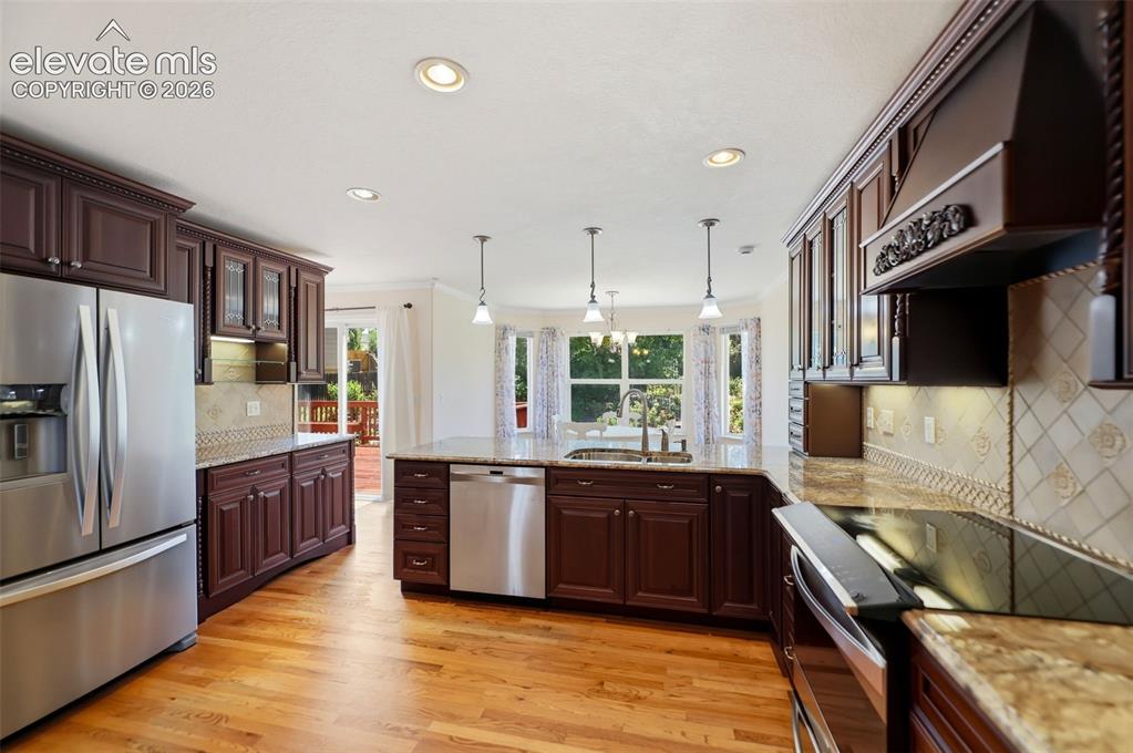 Image 8 of 50: Kitchen featuring wood-finish flooring, dark wood cabinetry, stainless stee