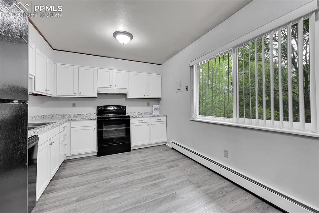 Image 25 of 33: Kitchen with baseboard heating, black appliances, white cabinets, light sto