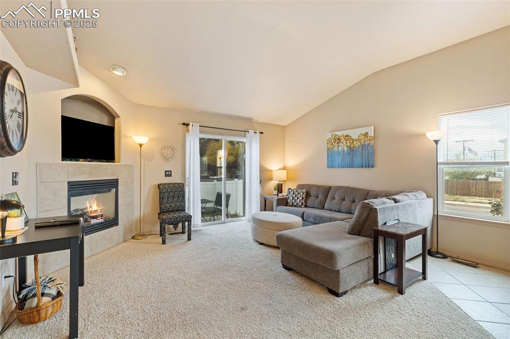 Image 5 of 27: Living area with lofted ceiling, a tiled fireplace, light colored carpet, a