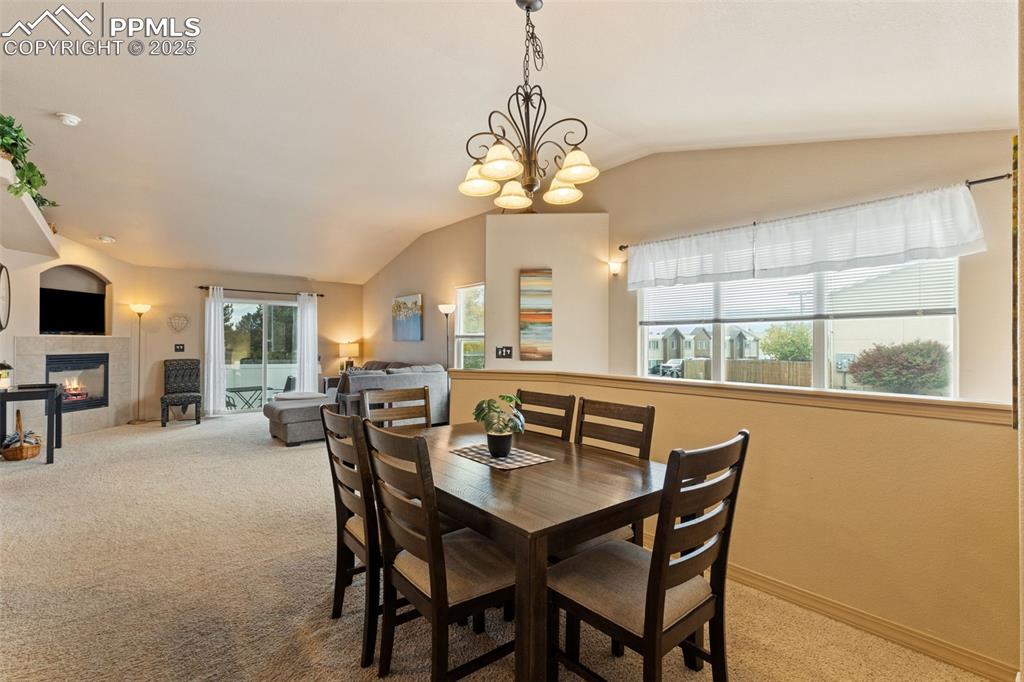 Image 7 of 27: Dining room with light colored carpet, vaulted ceiling, a tiled fireplace,
