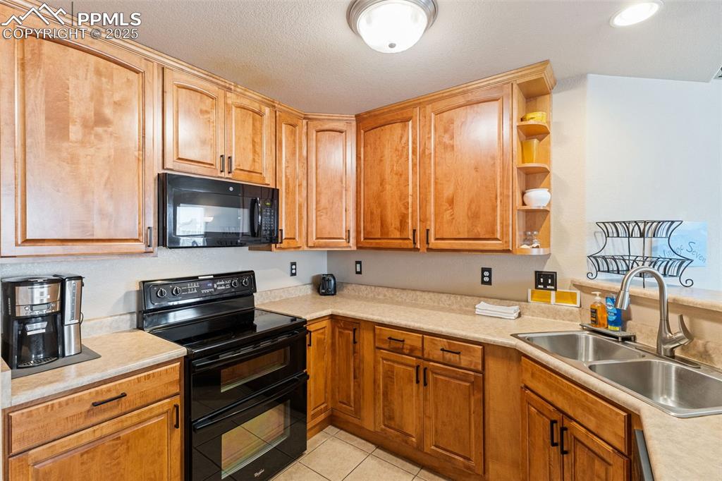 Image 9 of 27: Kitchen with black appliances, open shelves, light countertops, light tile