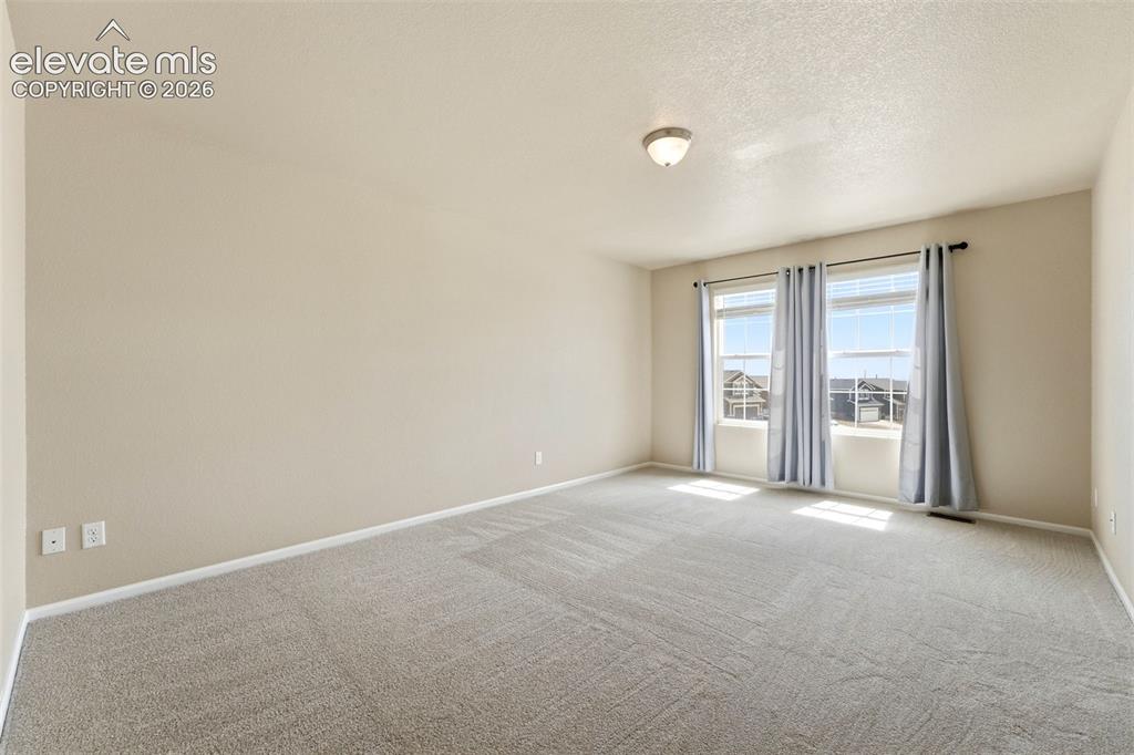 Image 18 of 33: Expansive room with neutral carpeting, two windows, and overhead lighting