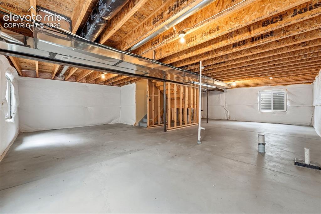 Image 25 of 33: Unfinished basement with exposed ceiling joists, concrete flooring, and par