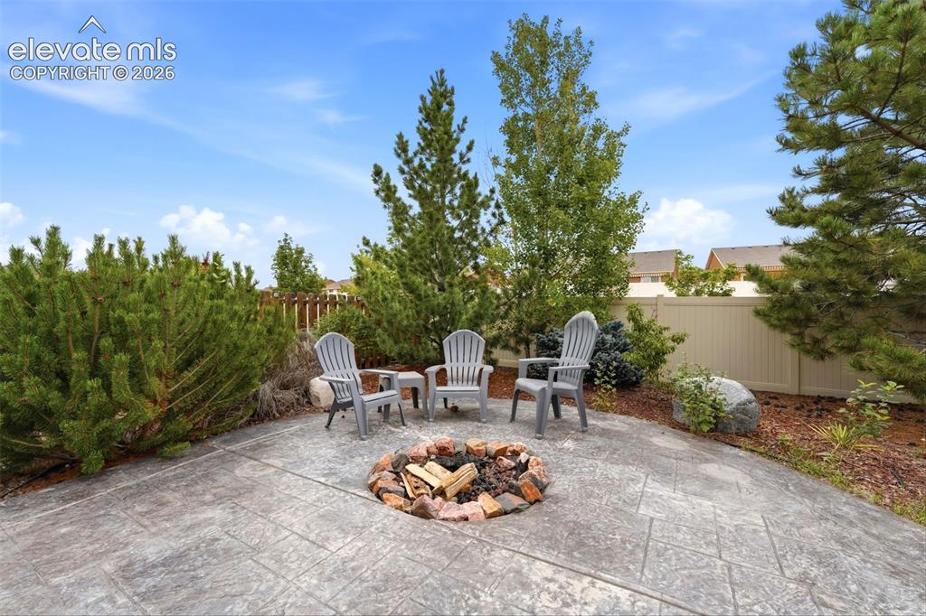 Image 27 of 33: Stamped concrete patio featuring a built-in stone fire pit, mature trees, a