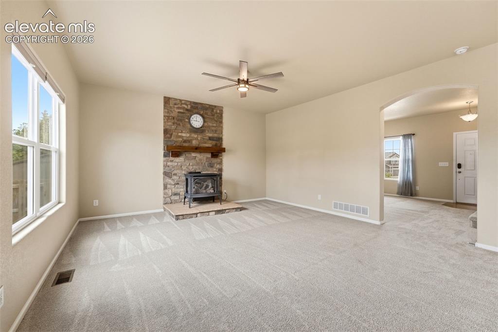 Image 6 of 33: Stone-finish fireplace with a wood mantle, ceiling fan, carpet flooring, ar