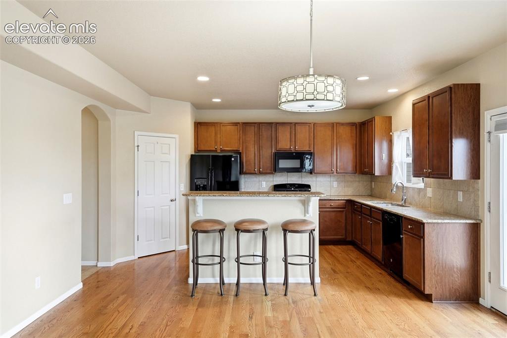 Image 8 of 33: Full kitchen featuring wood-finish flooring, dark wood cabinetry, a breakfa