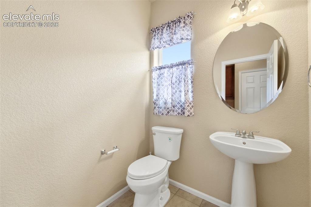 Image 9 of 33: Pedestal sink, wall-mounted mirror, ceramic toilet, and tiled flooring
