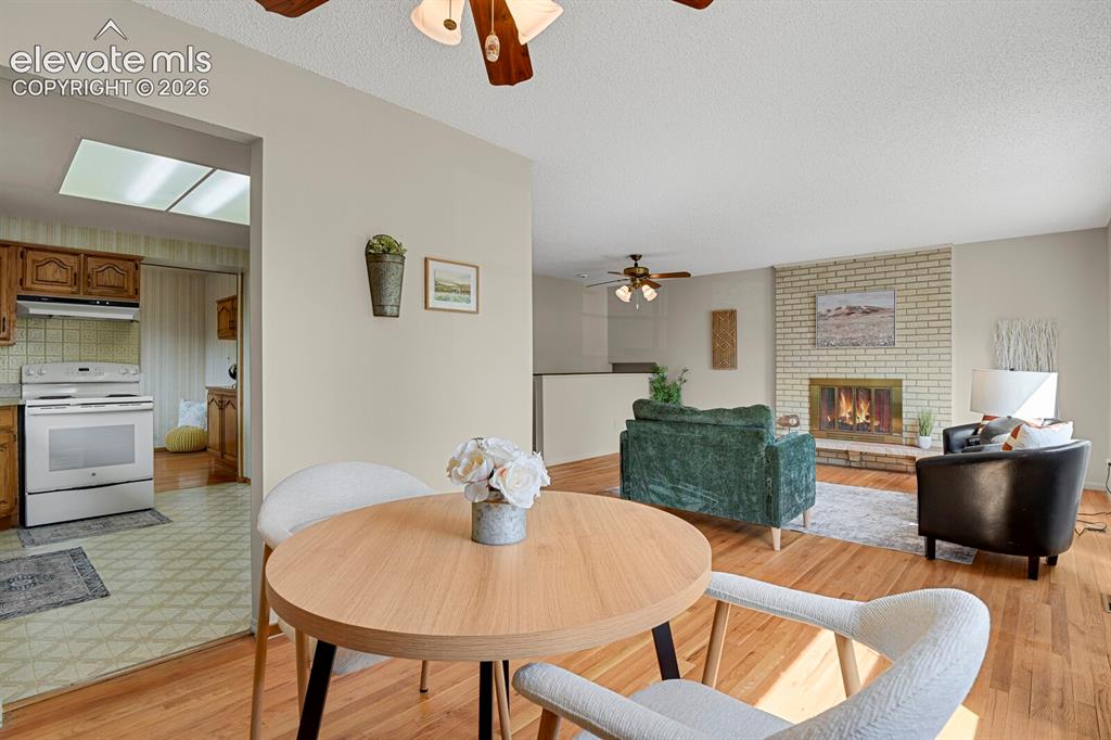 Image 15 of 48: Brick fireplace with golden firebox, wood-finish flooring, white kitchen ap