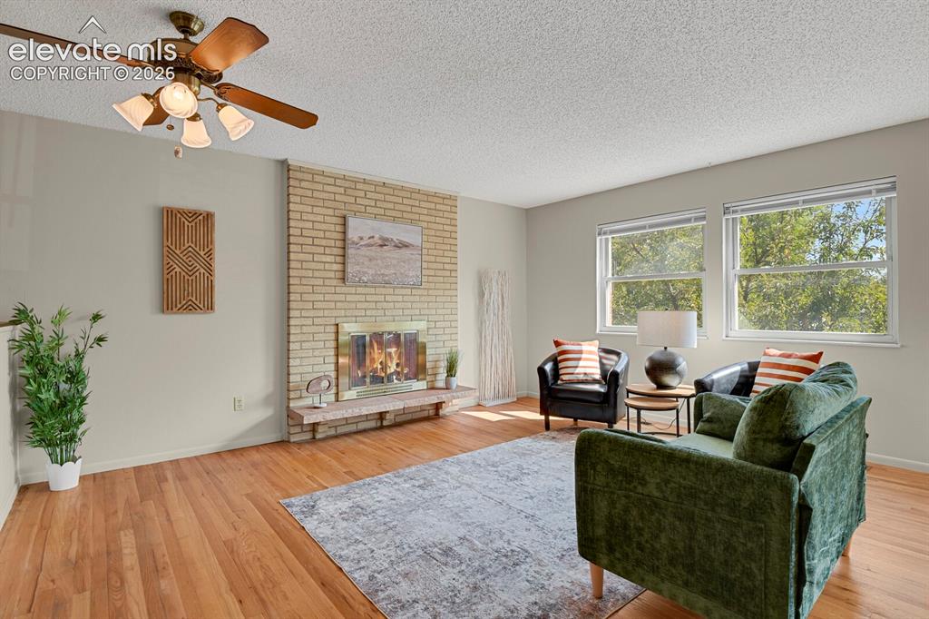 Image 8 of 48: Hardwood flooring, brick fireplace with hearth, multiple windows, ceiling f