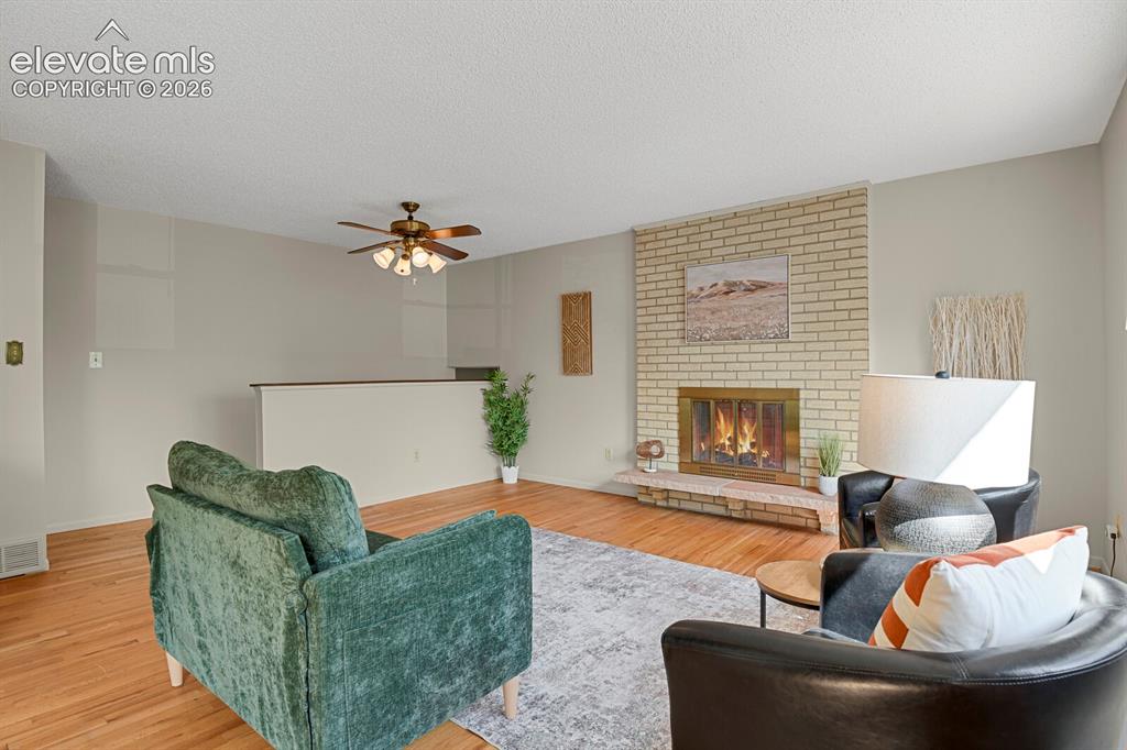 Image 9 of 48: Living area featuring a brick fireplace, hardwood flooring, and a ceiling f