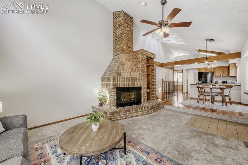 Image 5 of 34: Living area featuring light carpet, a ceiling fan, a fireplace, light tile 