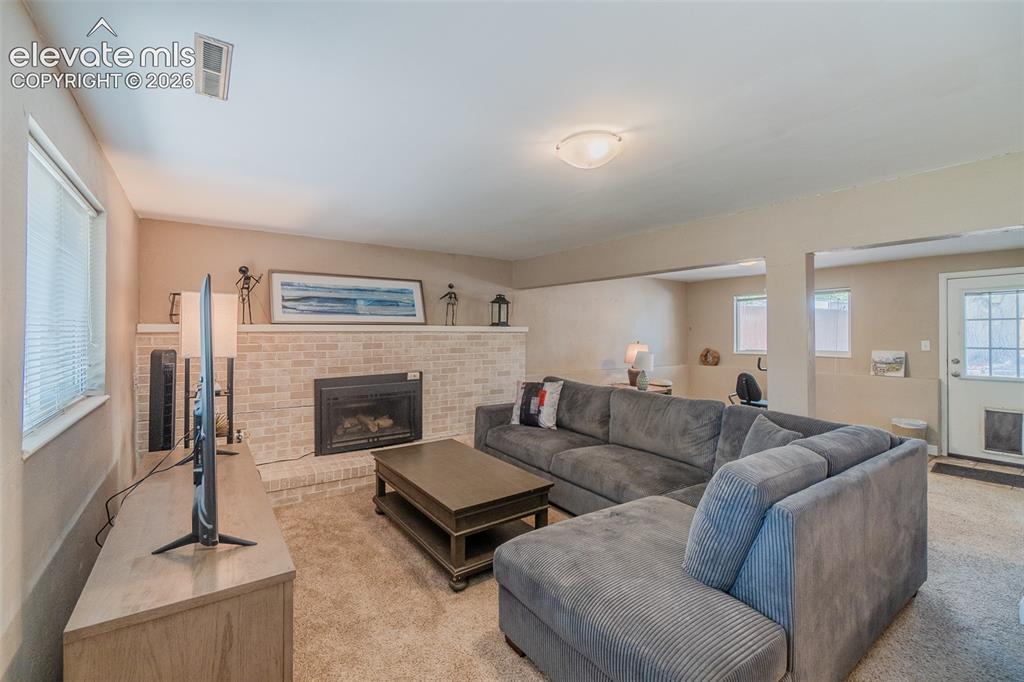 Image 11 of 30: Spacious living area featuring a light brick fireplace with hearth, plush c