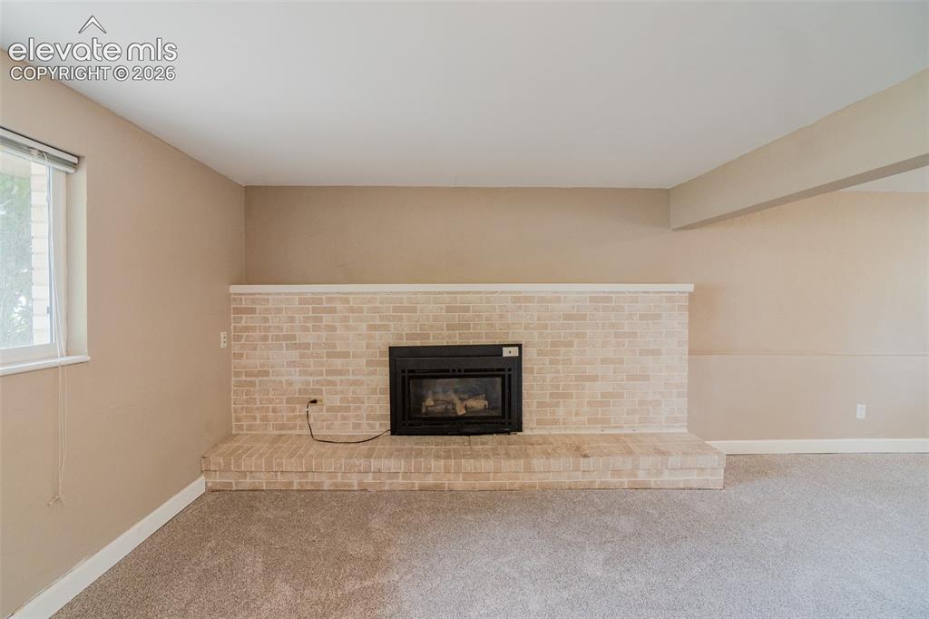 Image 12 of 42: Brick fireplace with a raised hearth, light-colored walls, and carpeting