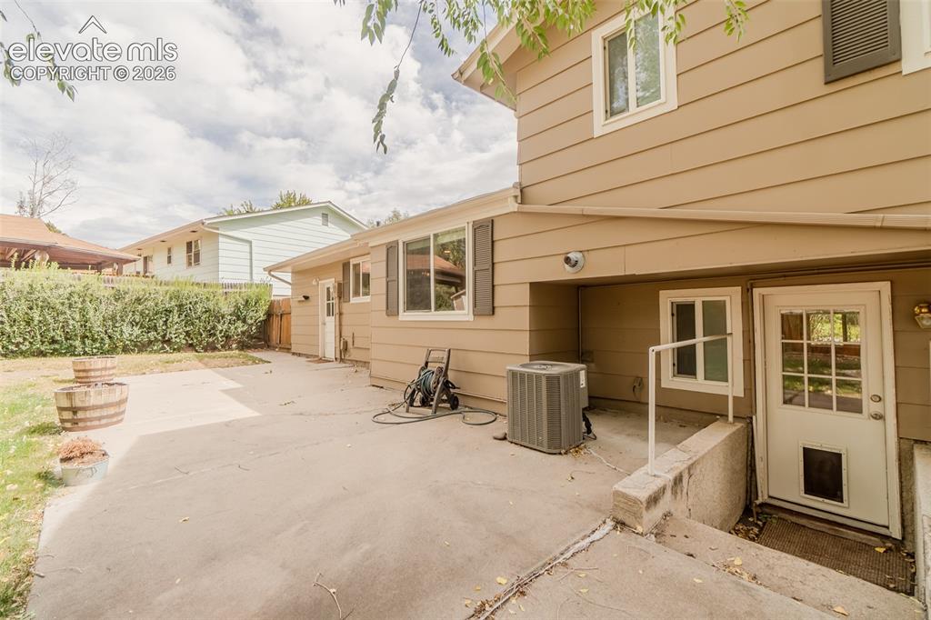 Image 15 of 42: Exterior featuring tan siding, a concrete patio, and a mature hedge