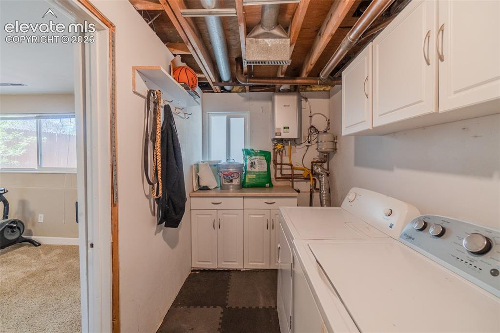 Image 26 of 30: Dedicated laundry area with tankless water heater, countertop with white ca