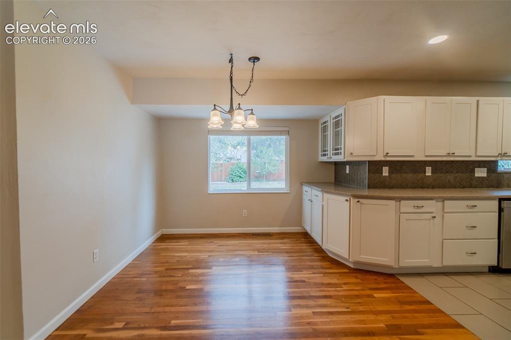 Image 41 of 42: Wood-finish flooring, white cabinetry, dark countertop, tile backsplash, an