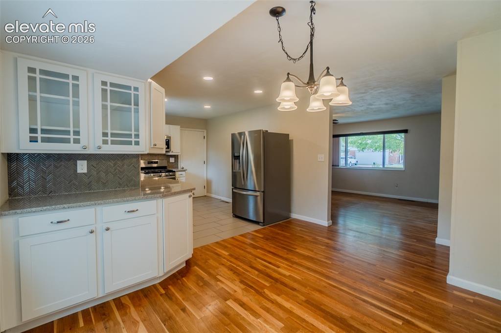 Image 6 of 42: Kitchen featuring white cabinetry, glass-front upper cabinets, patterned ti