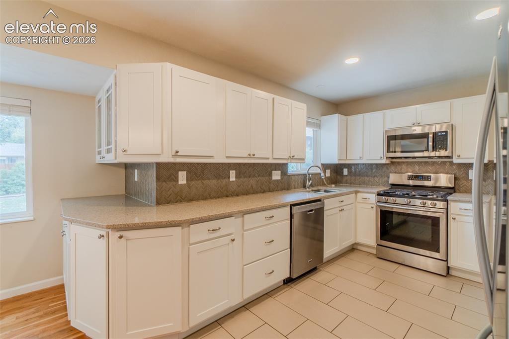 Image 7 of 42: White cabinetry, stainless steel appliances, tiled backsplash, light-toned