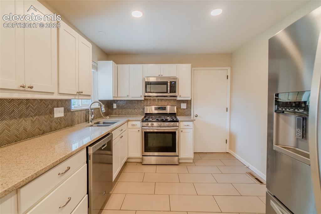 Image 8 of 42: White cabinetry, stainless steel appliances, patterned tile backsplash, lig