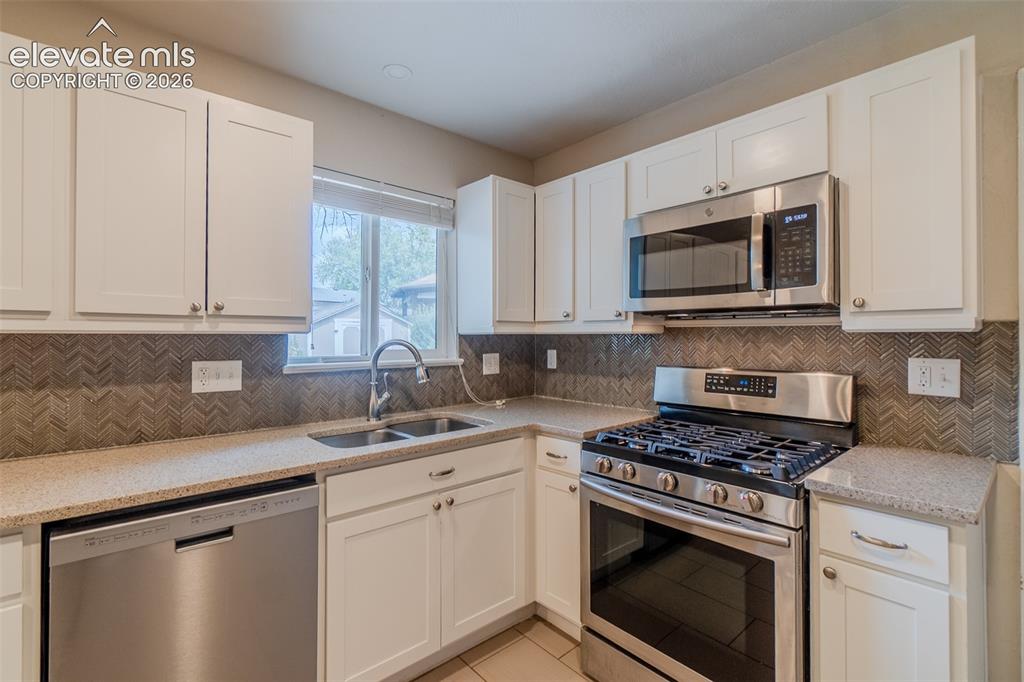 Image 9 of 42: White shaker cabinetry, stainless steel appliances, patterned tile backspla