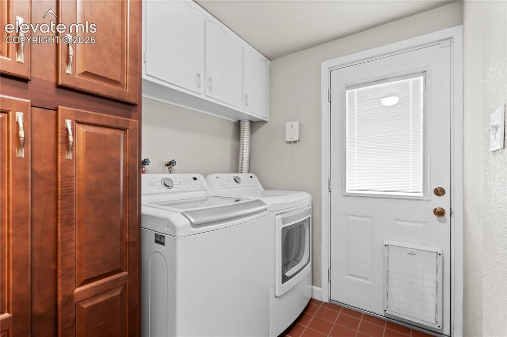 Image 31 of 31: Laundry area featuring wood-finish cabinetry, white upper cabinets, terraco
