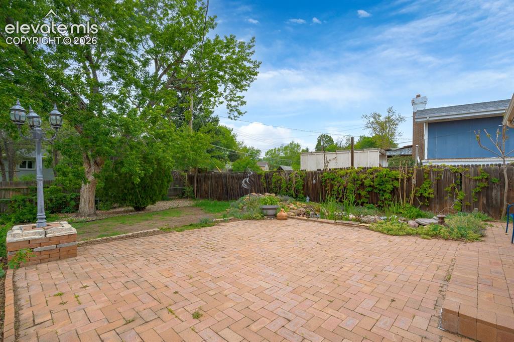 Image 6 of 31: Expansive brick paver patio with a decorative lamppost, surrounded by matur