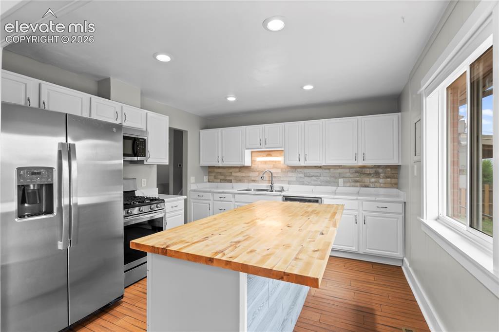 Image 7 of 31: Kitchen featuring a wood-finish island countertop, white cabinetry, stainle
