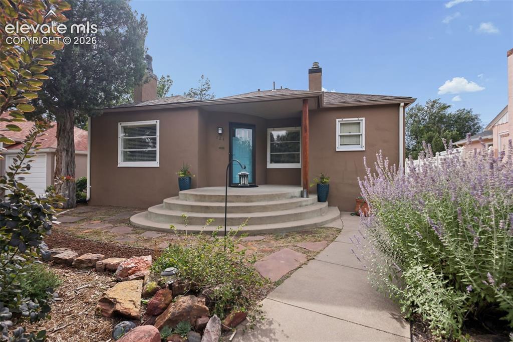 Caption: Stucco exterior with a covered entry, concrete steps, and a stone pathway