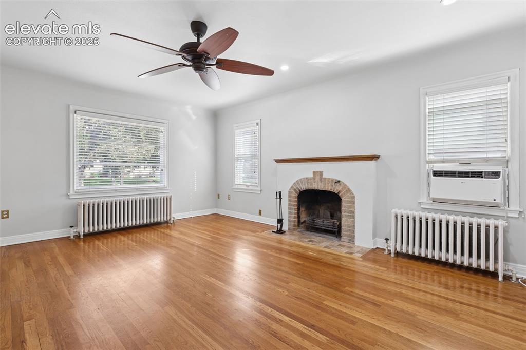 Image 10 of 50: Hardwood flooring, brick fireplace with mantel, ceiling fan, and multiple w