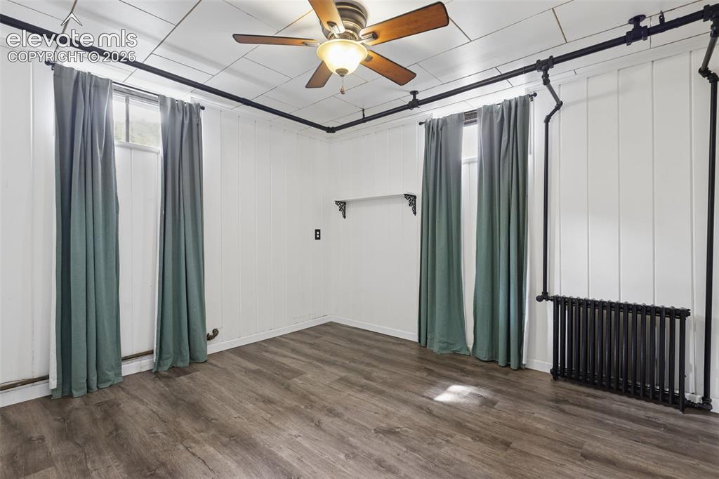 Image 28 of 50: Wood-finish flooring, white paneled walls, and a ceiling fan with integrate