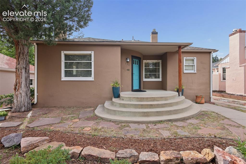 Image 3 of 50: Stucco exterior with a covered entry, round concrete steps, and a bold blue