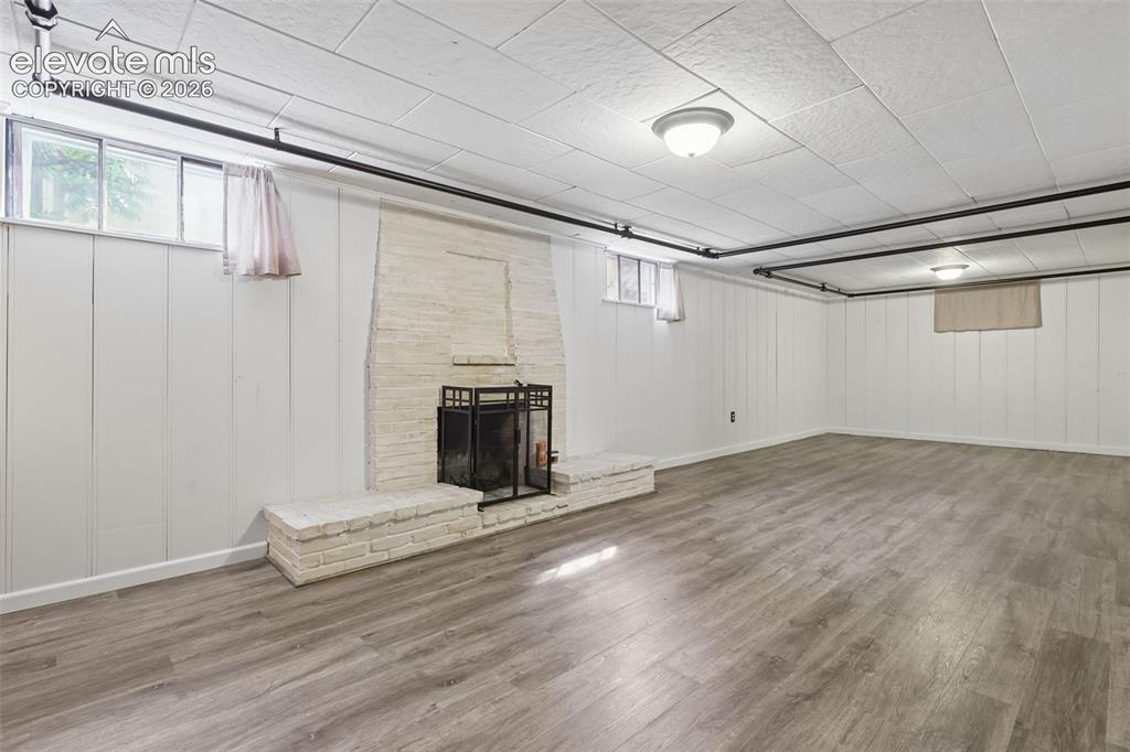 Image 30 of 50: Wood-finish flooring, white paneling, and a painted brick fireplace with a