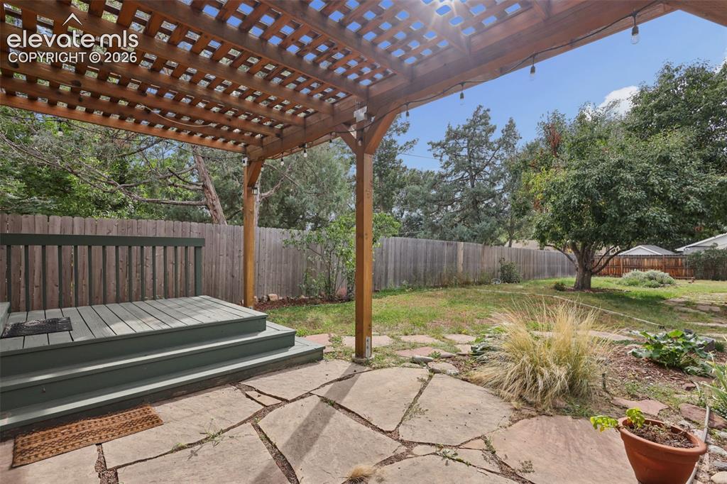 Image 38 of 50: Wood lattice pergola covering a stone patio, a two-tier wood deck, and a fe