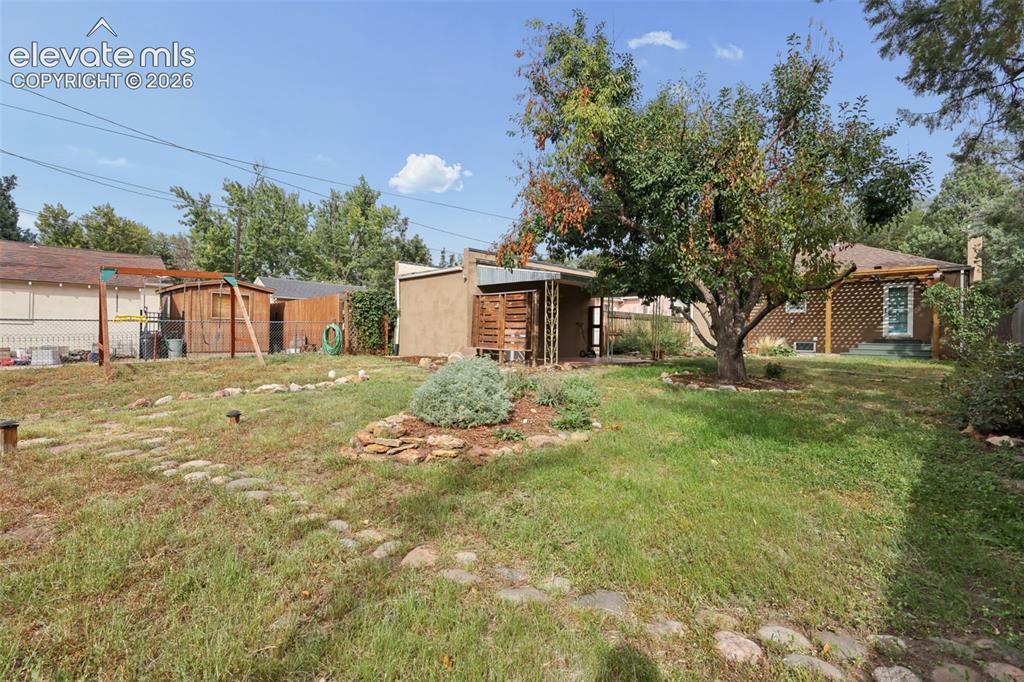Image 39 of 50: Expansive backyard featuring a large tree, stone-lined pathways, and a deta