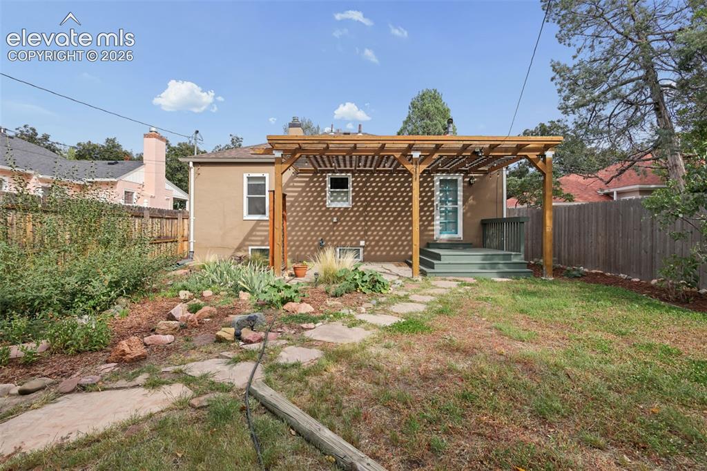 Image 42 of 50: Rear exterior featuring a wooden pergola, wood deck, and a stone pathway