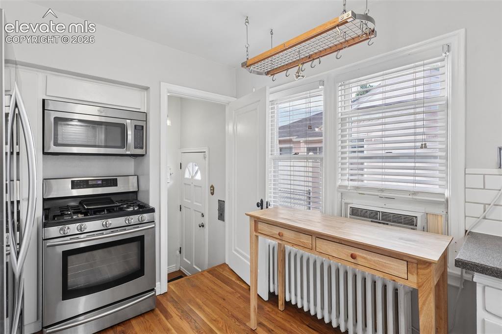 Image 5 of 50: Stainless steel appliances, wood-finish flooring, white cabinetry, and a po