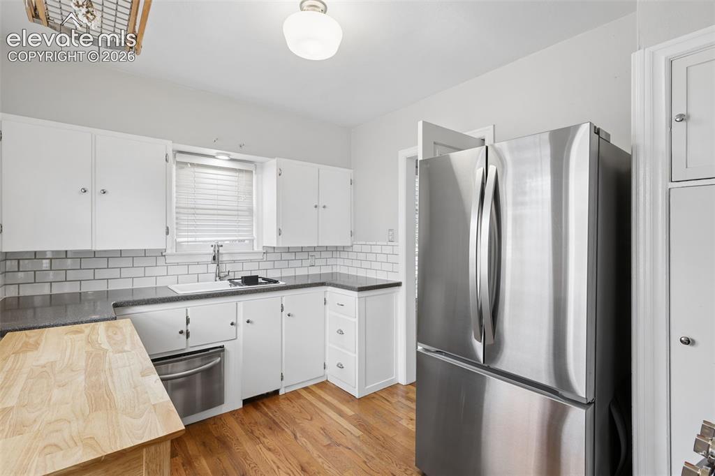 Image 7 of 50: Kitchen featuring wood-finish flooring, white cabinetry, subway tile backsp